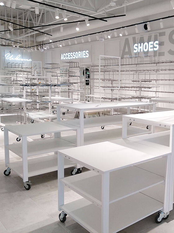 White freestanding display tables and wall shelving in a retail space