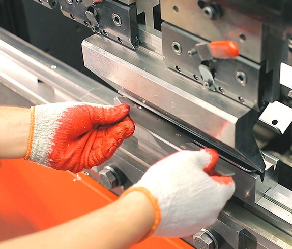 Gloved hands positioning sheet metal at forming equipment